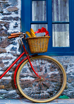 red bicycle leaning beneath a blue window. Red tulips and baguettes in basket.