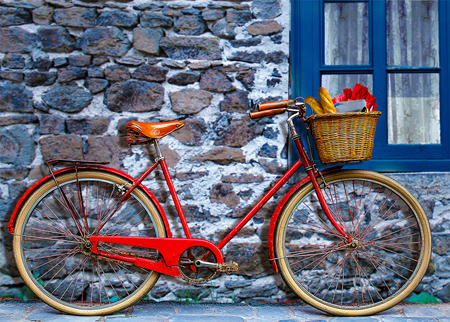 Red bicycle leaning against wall with tulips and baguettes in it's basket.